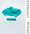 Close up view of a single turquoise blood lancet in focus with a blurred pile of lancets in the background, isolated on a white surface 139292618