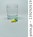 Front view of colorful medicine pills and a clear glass of water on a plain white background. 139292619