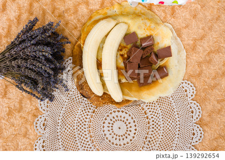 Pancakes with banana and chocolate pieces on a decorative placemat. Pancakes with banana and chocolate pieces on a decorative placemat. 139292654