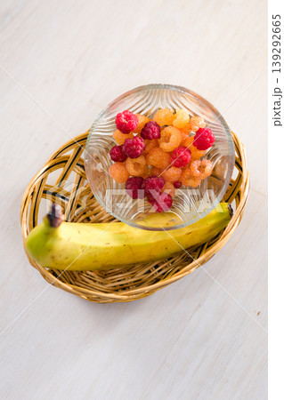 Fresh raspberries and a banana in a basket on a white table. Fresh raspberries and a banana in a basket on a white table. 139292665