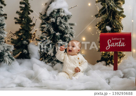 Snow simulation stuff on the ground. Little baby is sitting indoors in the Christmas decorated room Snow simulation stuff on the ground. Little baby is sitting indoors in the Christmas decorated room 139293688
