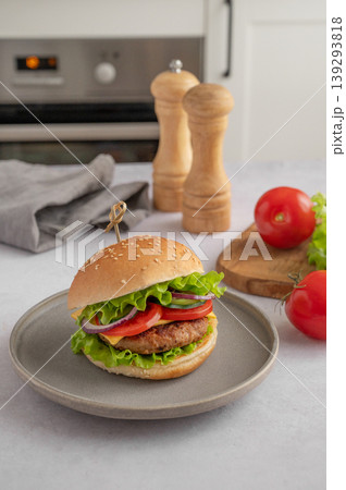 Beef burger with tomato, cheese, and lettuce on a plate on a kitchen table with spice Beef burger with tomato, cheese, and lettuce on a plate on a kitchen table with spice 139293818
