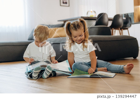 Reading interesting magazine or book. Little kids are playing together in the domestic room at daytime Reading interesting magazine or book. Little kids are playing together in the domestic room at daytime 139294447