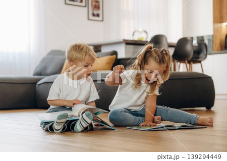 Reading interesting magazine or book. Little kids are playing together in the domestic room at daytime Reading interesting magazine or book. Little kids are playing together in the domestic room at daytime 139294449