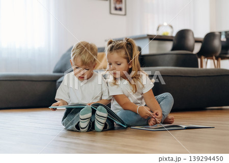 Reading interesting magazine or book. Little kids are playing together in the domestic room at daytime Reading interesting magazine or book. Little kids are playing together in the domestic room at daytime 139294450
