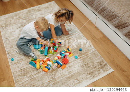 Red, blue, yellow colored objects. Two kids are playing with construction blocks toys at home Red, blue, yellow colored objects. Two kids are playing with construction blocks toys at home 139294468