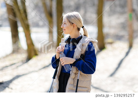 Young woman nordic walking in forest during winter sunny day Young woman nordic walking in forest during winter sunny day 139295257