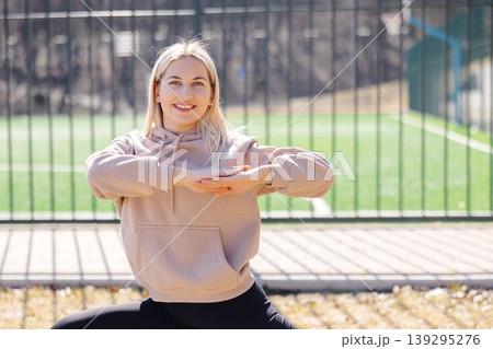Young woman performing yoga exercises in a park near a soccer field 139295276