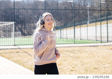 Young sporty woman jogging while listening to music with headphones in a sports center Young sporty woman jogging while listening to music with headphones in a sports center 139295280