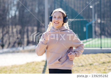 Young sportswoman running in the park listening music with headphones Young sportswoman running in the park listening music with headphones 139295282