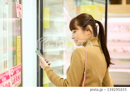スマートフォンを見ながらスーパーで買い物をする女性 スマートフォンを見ながらスーパーで買い物をする女性 139295835