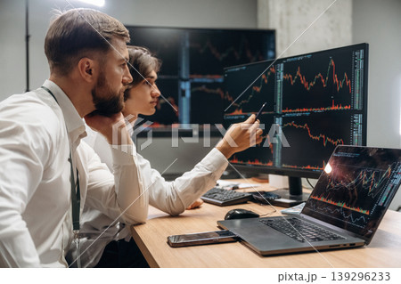 Crypto and stock graphs are on the screens. Two male exchange workers are in the office together Crypto and stock graphs are on the screens. Two male exchange workers are in the office together 139296233