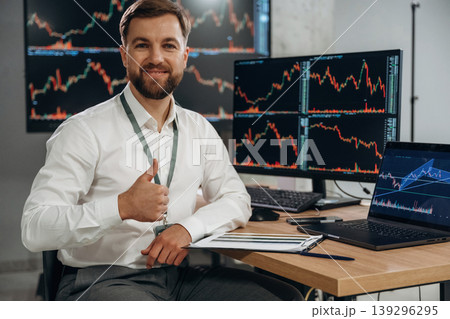 The document is in notepad. Handsome businessman is in the office with stock exchange market information on displays The document is in notepad. Handsome businessman is in the office with stock exchange market information on displays 139296295