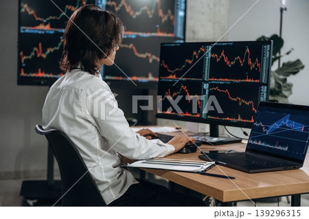 Real time monitoring graphs are on the screens. Young man is sitting in the office with multiple displays of stock market data Real time monitoring graphs are on the screens. Young man is sitting in the office with multiple displays of stock market data 139296315