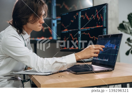 Real time monitoring graphs are on the screens. Young man is sitting in the office with multiple displays of stock market data Real time monitoring graphs are on the screens. Young man is sitting in the office with multiple displays of stock market data 139296321