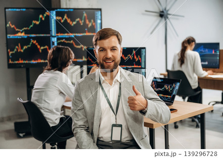 Beautiful man is standing in front of colleagues. Business people are working with stock market exchange in office Beautiful man is standing in front of colleagues. Business people are working with stock market exchange in office 139296728