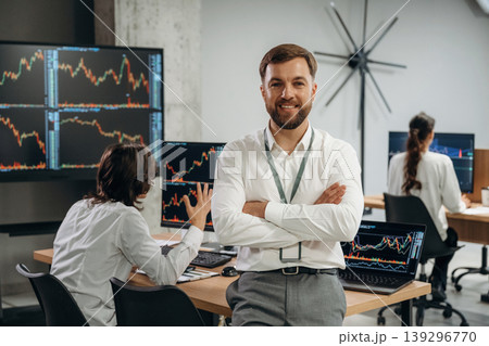 Arms crossed, man is standing. Business people are working with stock market exchange in office Arms crossed, man is standing. Business people are working with stock market exchange in office 139296770