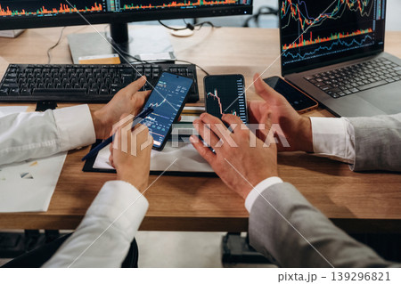 Comparing the data. Close up view of hands of business men that are working with stock market exchange Comparing the data. Close up view of hands of business men that are working with stock market exchange 139296821