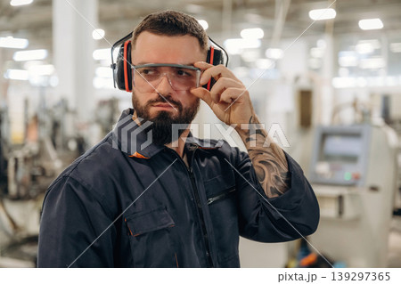 Posing, standing in protective eyewear. Warehouse worker in an industrial environment of a factory or storage area Posing, standing in protective eyewear. Warehouse worker in an industrial environment of a factory or storage area 139297365