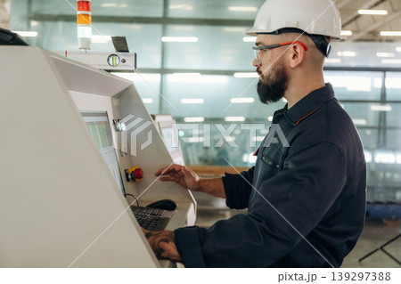 Side view, machine operator is standing and working. Warehouse worker in an industrial environment of a factory or storage area Side view, machine operator is standing and working. Warehouse worker in an industrial environment of a factory or storage area 139297388