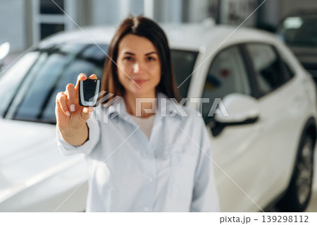 Ready to drive, showing keys. Woman posing with a car in an auto showroom, modern dealership environment Ready to drive, showing keys. Woman posing with a car in an auto showroom, modern dealership environment 139298112