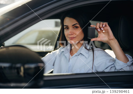 Through the window, holding keys. Woman is sitting in the modern car, happy new owner Through the window, holding keys. Woman is sitting in the modern car, happy new owner 139298461