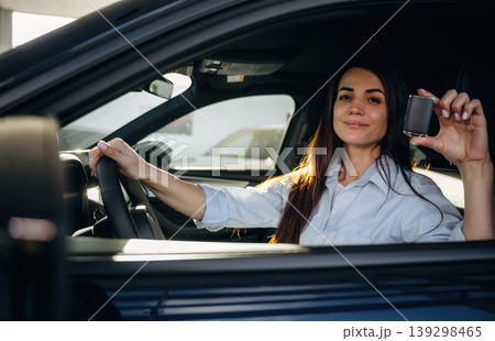 Proud owner is holding the keys. Woman is sitting in the modern car, happy new owner Proud owner is holding the keys. Woman is sitting in the modern car, happy new owner 139298465