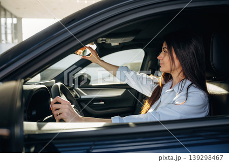 Adjusting the mirror. Woman is sitting in the modern car, happy new owner 139298467