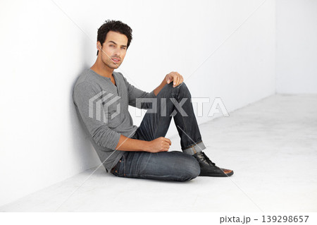 Serious, fashion and portrait of young man by white wall with casual, stylish and trendy outfit. Attractive, confidence and handsome male model from Canada sitting on floor with edgy and cool style. 139298657
