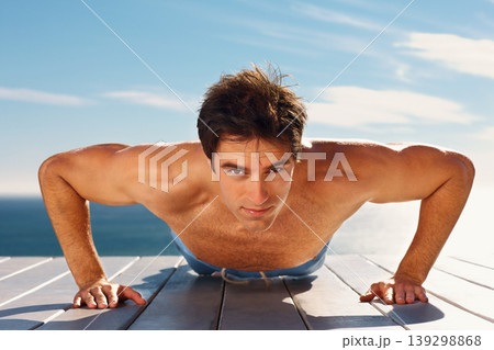 Young man, push up and portrait with workout for health body, fitness and exercise by sky background. Model, face and commitment with glow for wellness and muscle training on plank on summer vacation 139298868