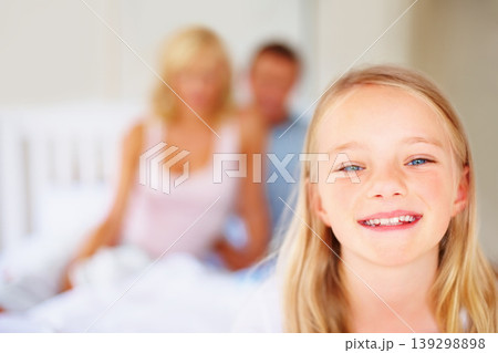 Portrait, smile and a girl in the bedroom of a home with her parents in the background to relax on a weekend. Face, kids and a happy young child on a bed in an apartment to wake up in the morning Portrait, smile and a girl in the bedroom of a home with her parents in the background to relax on a weekend. Face, kids and a happy young child on a bed in an apartment to wake up in the morning 139298898