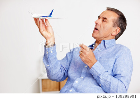 Mature man, flying and toy plane for travel, vacation and holiday planning with a smile at home. Happy, airplane model and retirement of a male person with confidence from trip and air traveling Mature man, flying and toy plane for travel, vacation and holiday planning with a smile at home. Happy, airplane model and retirement of a male person with confidence from trip and air traveling 139298901