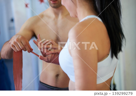 Coach, woman and wrap hands for boxing workout exercise, fight practice at punch club. Man, client and wrist support or tape for healthy fist or athlete bandage for gym sports, challenge for defense Coach, woman and wrap hands for boxing workout exercise, fight practice at punch club. Man, client and wrist support or tape for healthy fist or athlete bandage for gym sports, challenge for defense 139299279
