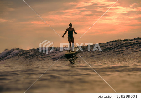 Graceful Female Surfer Maintains Poised Stance During Sunset Surf Graceful Female Surfer Maintains Poised Stance During Sunset Surf 139299601
