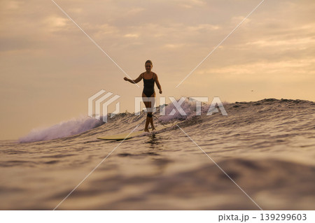 Confident Female Surfer Calmly Handles Gentle Coastal Surf At Dusk 139299603