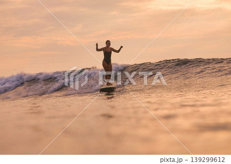Relaxed Female Enjoying Peaceful Surfboard Ride During Sunset Relaxed Female Enjoying Peaceful Surfboard Ride During Sunset 139299612
