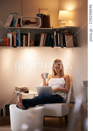 Woman, laptop and reading with coffee at night on chair in relax or living room at home. Female person, journalist or bookworm sitting with cup of tea and computer for online connection at house 139299646