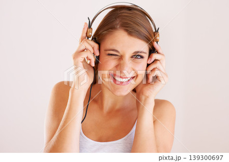 Woman, portrait and wink with headphones in studio for music, audio subscription or streaming multimedia album on white background. Happy model, blink and listening to podcast, hearing sound or radio Woman, portrait and wink with headphones in studio for music, audio subscription or streaming multimedia album on white background. Happy model, blink and listening to podcast, hearing sound or radio 139300697