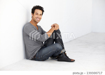 Smile, fashion and portrait of young man by a white wall in empty room with casual, cool and trendy outfit. Happy, confidence and handsome male model from Canada sitting on floor with edgy style. Smile, fashion and portrait of young man by a white wall in empty room with casual, cool and trendy outfit. Happy, confidence and handsome male model from Canada sitting on floor with edgy style. 139300717