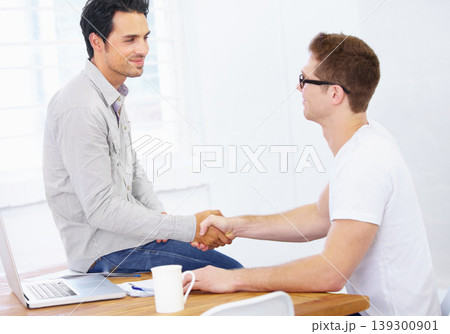 Business men, handshake and agreement at desk in office to offer promotion, support deal and success in creative agency. Team shaking hands for negotiation, onboarding or trust for design partnership Business men, handshake and agreement at desk in office to offer promotion, support deal and success in creative agency. Team shaking hands for negotiation, onboarding or trust for design partnership 139300901