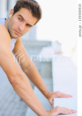 Fitness, earphones and young man athlete by a wall for running listening to music, playlist or album. Sports, workout and male runner training with cardio exercise in street in the city with podcast. Fitness, earphones and young man athlete by a wall for running listening to music, playlist or album. Sports, workout and male runner training with cardio exercise in street in the city with podcast. 139300910