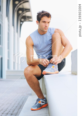 Man, fitness and tying shoes getting ready for workout, exercise or outdoor training with earphones. Active male person or athlete tie shoe on concrete bench in preparation for run or cardio outside Man, fitness and tying shoes getting ready for workout, exercise or outdoor training with earphones. Active male person or athlete tie shoe on concrete bench in preparation for run or cardio outside 139301004