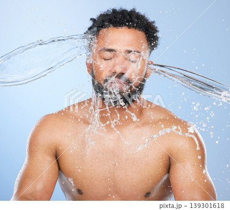 Black man, water splash and washing in skincare for cleaning, hygiene or grooming against a blue studio background. Face of African male person, model and aqua for body hydration, shower or skin wash Black man, water splash and washing in skincare for cleaning, hygiene or grooming against a blue studio background. Face of African male person, model and aqua for body hydration, shower or skin wash 139301618