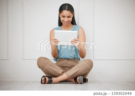 Tablet, smile and business woman by the wall networking on social media, mobile app or the internet. Happy, digital technology and young female person scroll on website sitting on the floor in space. 139302049