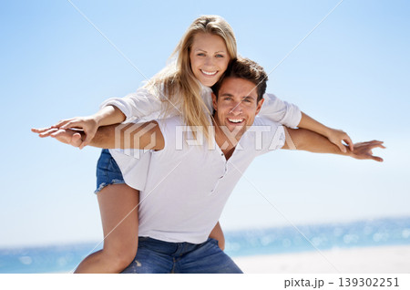 Couple, beach and happy for piggy back in portrait, vacation or freedom in summer sunshine for bonding. Man, woman and plane game with smile, care or love by sand, waves or play on holiday in Napoli 139302251