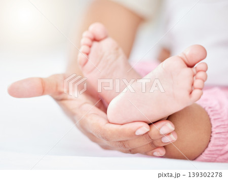 Family, love and the feet of a baby in the hands of a parent closeup in the bedroom of their home together. Kids, care or wellness and an infant child on a bed in an apartment with an adult person 139302278