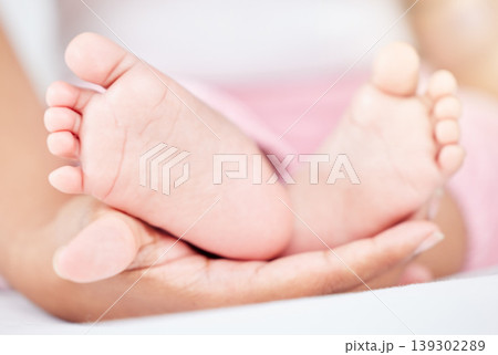 Family, care and the feet of a baby in the hands of a parent closeup in the bedroom of their home together. Kids, love or wellness and an infant child on a bed in an apartment with an adult person 139302289