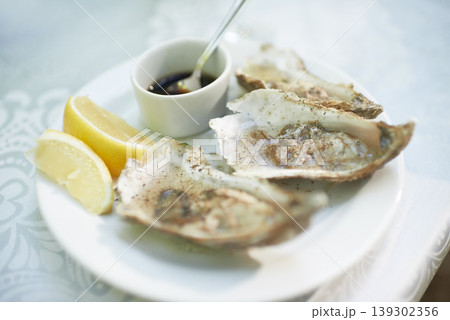 Background, food and plate of oysters in restaurant for lunch, dinner and eating appetizer of gourmet cuisine. Closeup, luxury seafood diner and serving of healthy shellfish dish on table with lemon Background, food and plate of oysters in restaurant for lunch, dinner and eating appetizer of gourmet cuisine. Closeup, luxury seafood diner and serving of healthy shellfish dish on table with lemon 139302356