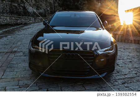 Black Audi luxury sedan car parked on an cobblestone road with sunset on the background 139302554