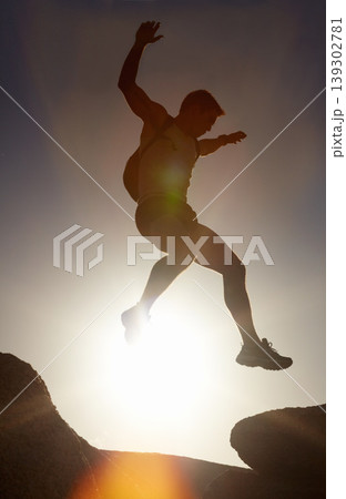 Man, silhouette and jump on rock at sunset with freedom, adventure and challenge on mountain or cliff. Climbing, hill and person with fearless leap in hiking, exercise or energy at with sky in summer 139302781